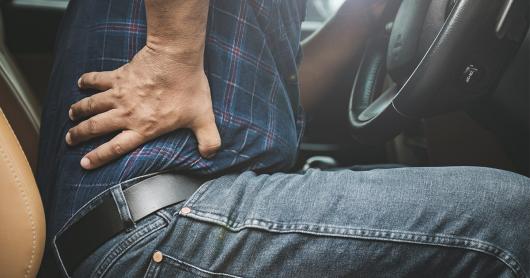 a man holds back in pain, sitting in a stationary car