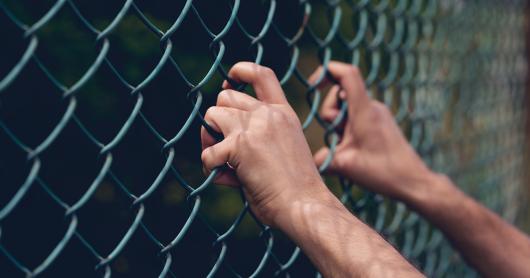 Young person's hand holding onto a chain link fence