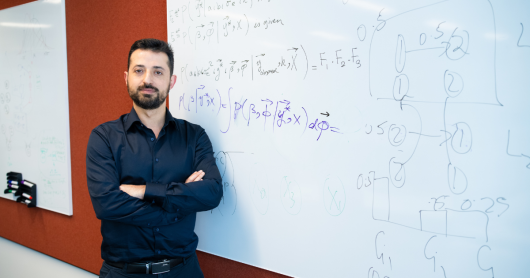Man with arms folded standing in front of whiteboard with formulas on it