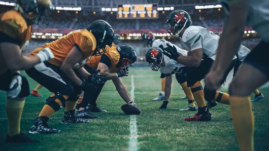 Two teams face off in an American football match. Picture by Gorodenkoff, Adobe Stock