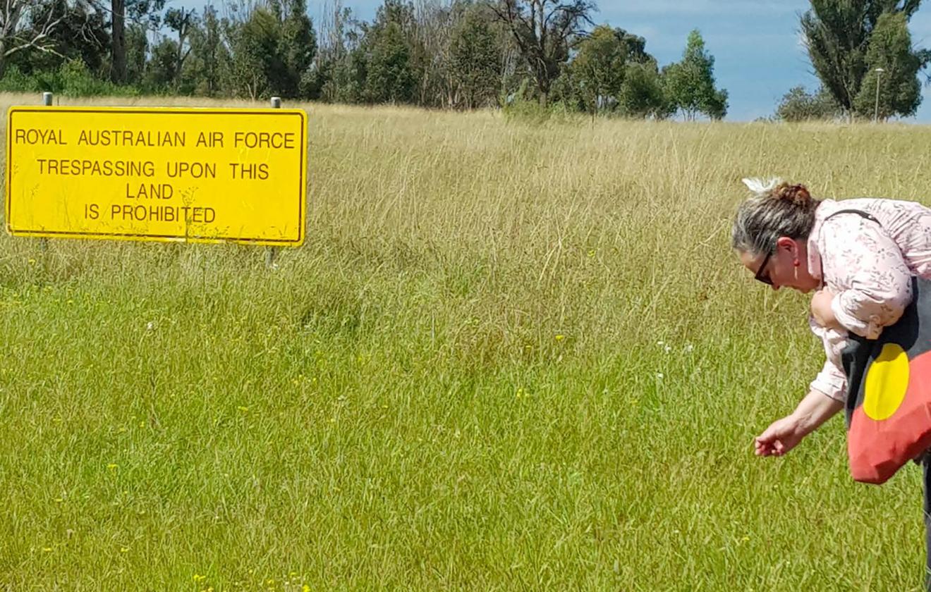 woman in meadow with sign reading royal australian air force trespassing upon this land is prohbitied