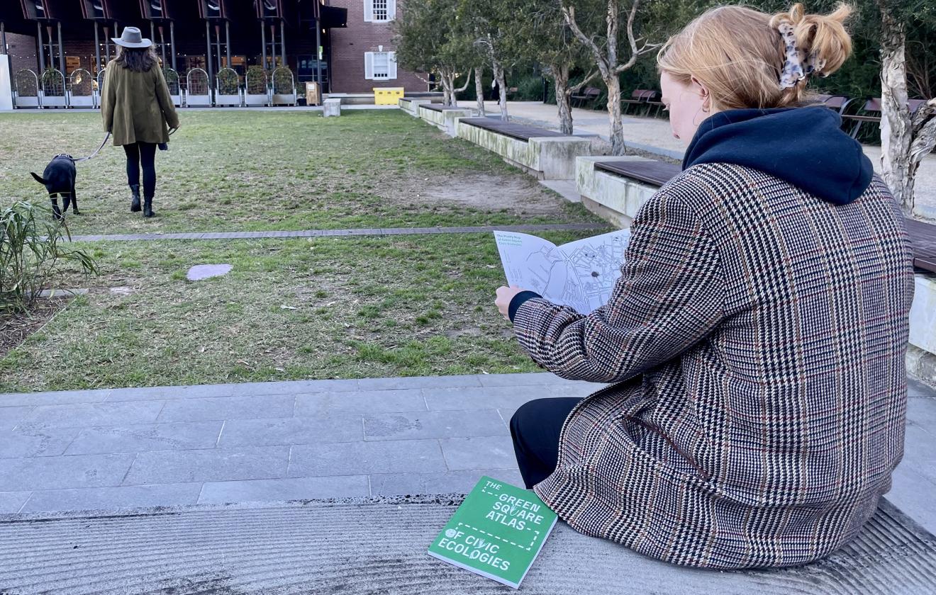 Woman sitting on bench reading the green square atlas