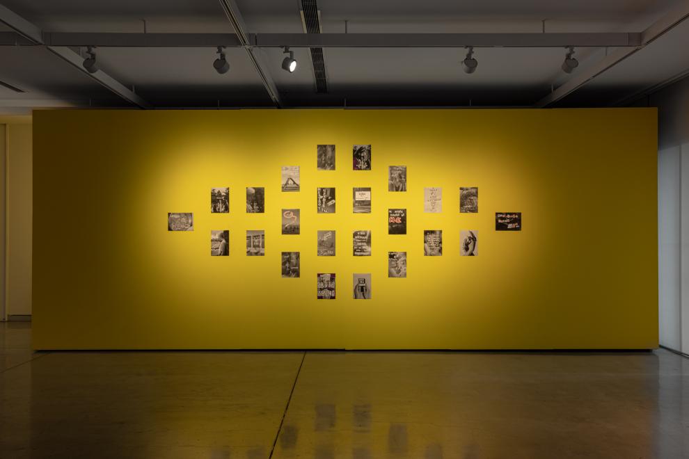 A series of black and white collages displayed on a yellow wall 
