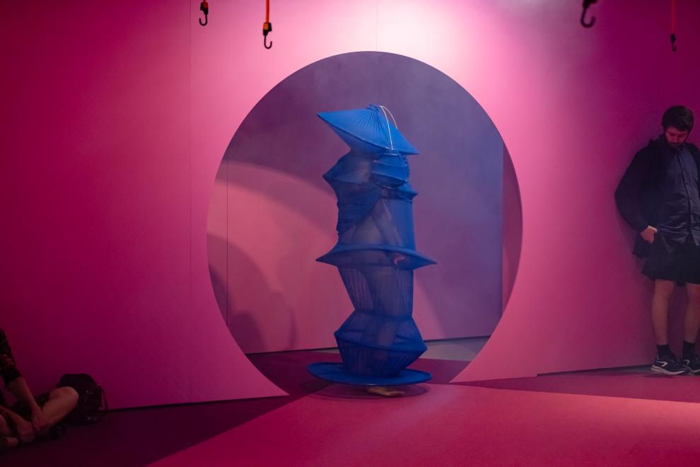 A person in a blue costume emerges from a round doorway painted pink