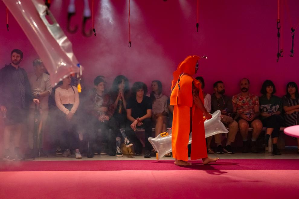 A person in an orange costume walks on a runway
