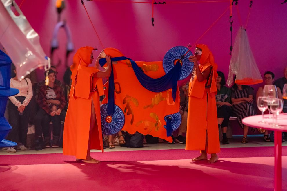 Two people in orange costumes hang another orange costume on octopus straps