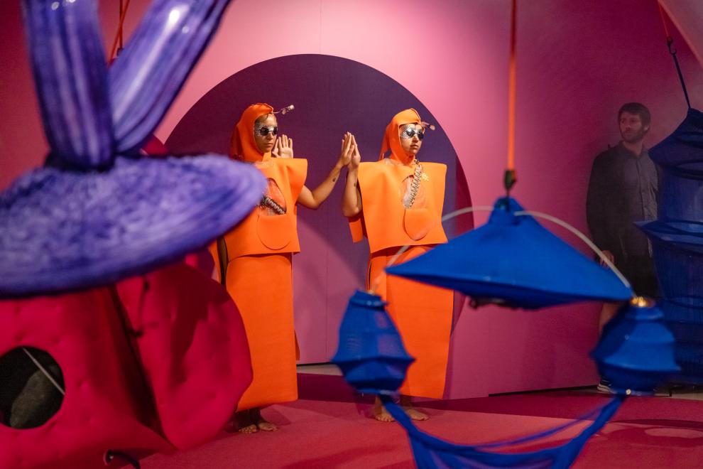 Two people in orange costumes hold hands in a rounded doorway