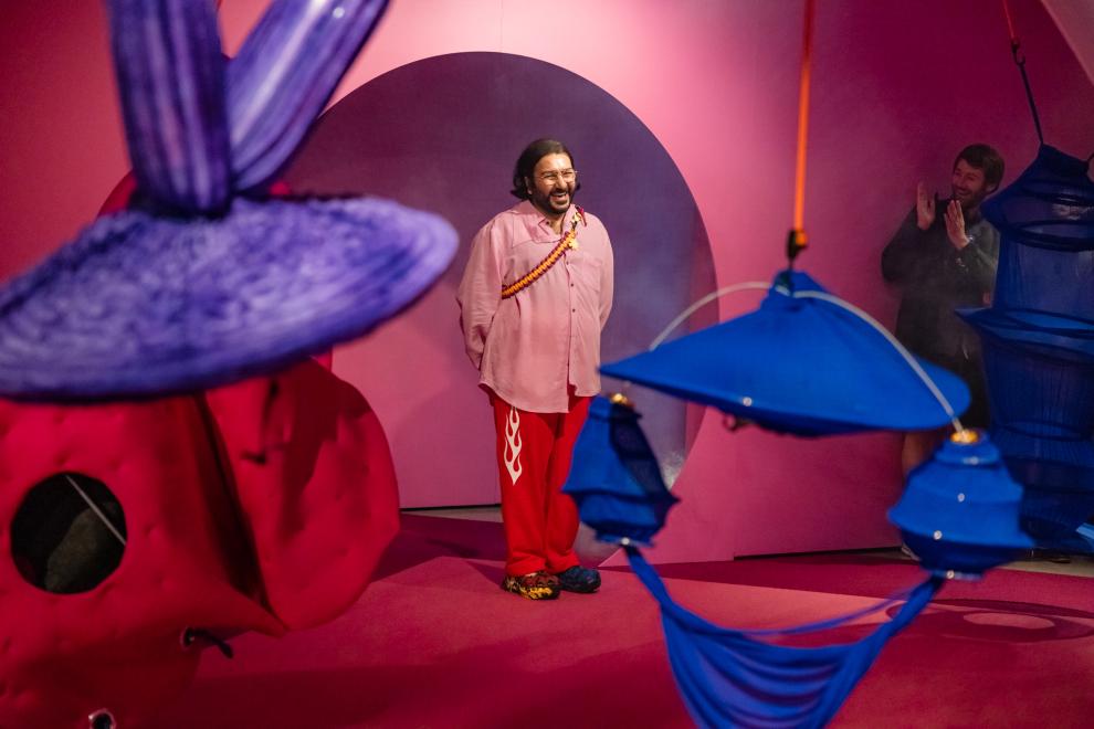 A person in a pink shirt gives a broad smile in a pink rounded doorway