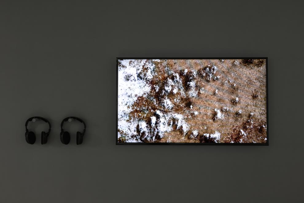 A tv monitor on a wall with two pairs of headphones. The tv shows an aerial view of a rocky landscape