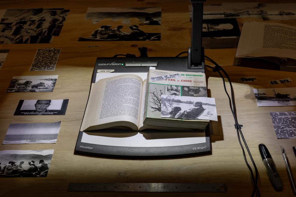 a sculptural installation by Prima Jalichandra-Sakuntabhai, which comprises a large timber table with carefully placed archival materials and a digital document camera which is projecting a collage of these materials onto the wall beside the table. 