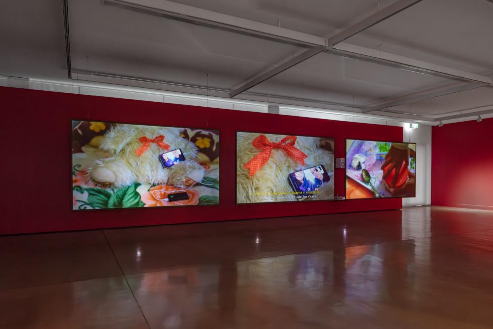 A three channel video work in a gallery with red walls 
