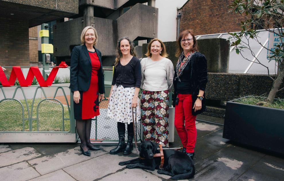 Four women stand in front of a fenced-off grass facility at the UTS city campus.