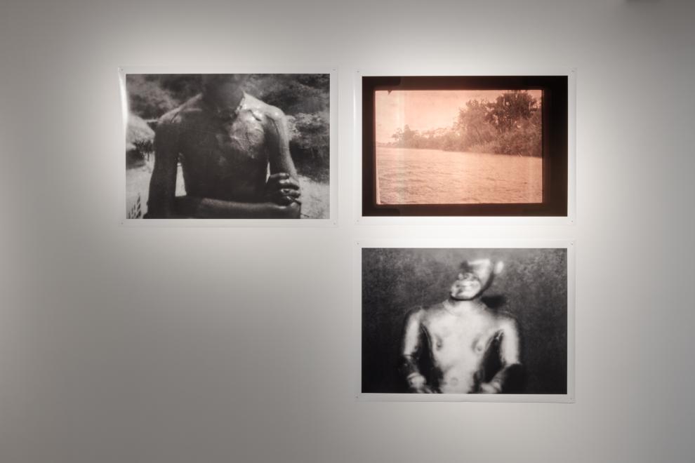 A photograph showing 3 large scale photographs of a pink-washed river scene, a mud-covered torso where the identifying head has been cropped out of the image, and a museum close-up of a burnished gold figurine from antiquity, that is blurred and falling into shadow. 