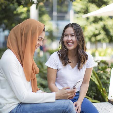 Two female undergraduate students laughing and looking at a phone