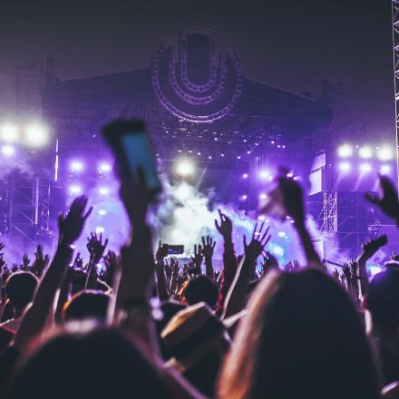 Large crowd of people with hands in the air at an outdoor concert, looking towards stage.