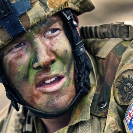 Head and shoulder view of Australian soldier with camouflage paint on face, wearing a helmet