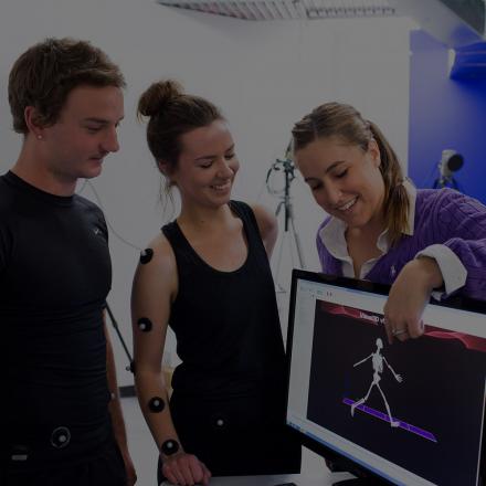 A woman wearing movement sensors looking at a computer image with 2 others