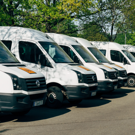 A row of parked white vans with trees in the background