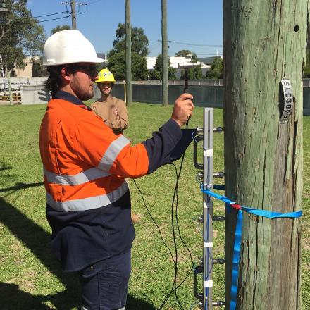 Man in hard had holds a device against a telegraph pole