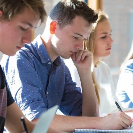 Three students (two males and one female) listening while taking notes