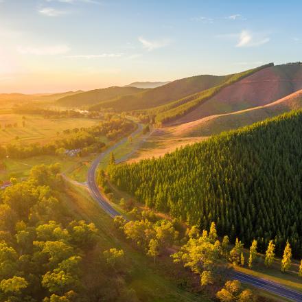 Green hills in the foreground with a blue sky and sun coming over the horizon