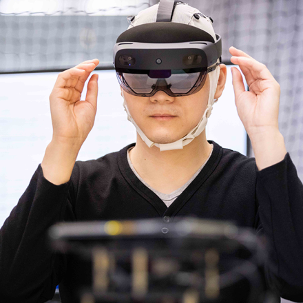 PhD student, Daniel Leong uses augmented reality (wears dark glasses and a headset) to control a BCI-enabled robot (faded in the foreground)