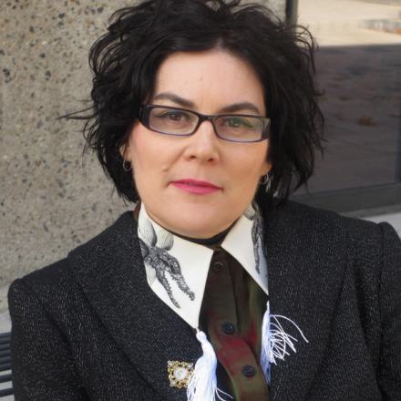 Woman smiling at camera. She has cropped short black hair and glasses.