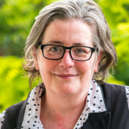 Woman smiling at camera. She has cropped streaked hair and glasses.