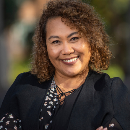 woman smiling at camera. She has curly, shoulder-length brown hair and is wearing black.