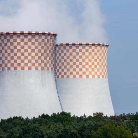 Two chimney stacks smoking with blue sky and trees in foreground