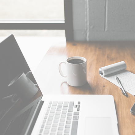 Laptop, coffee cup, notepad with pen, and phone