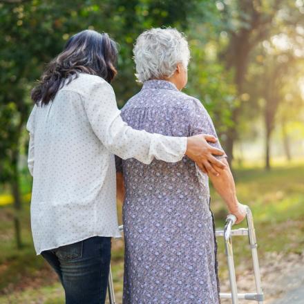 Woman helping elderly person walk outdoors