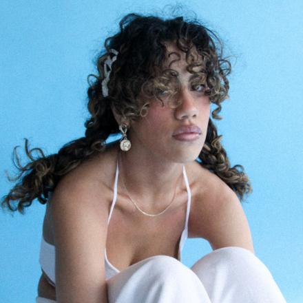 woman with curly hair wearing white sitting with knees up and her arms crossed under her knees