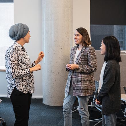 Three people standing talking to each other in a relaxed conversation in a room