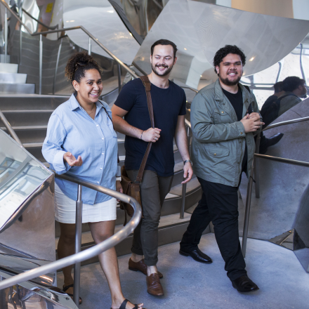 Three students are walking down a staircase and engaging in casual conversation.