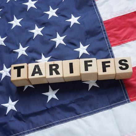 Blocks spelling out tariffs lie on an American flag