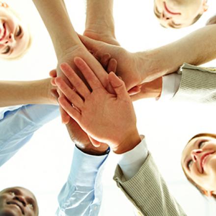 Four people in a circle with their hands placed together