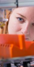 A female student inspects her bright orange additive 3D printed object