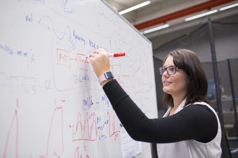 Female student writing on a white board in a lab