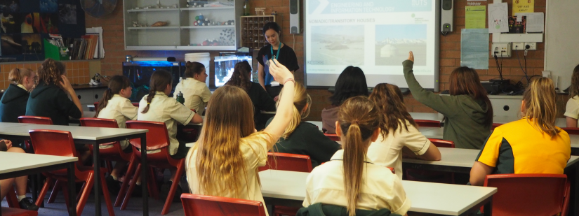 Students raise their hand to answer a question at a school visit