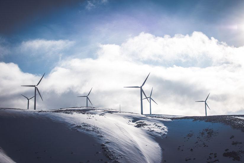 Windmills on top of a snowy mountain against a cloudy sky.