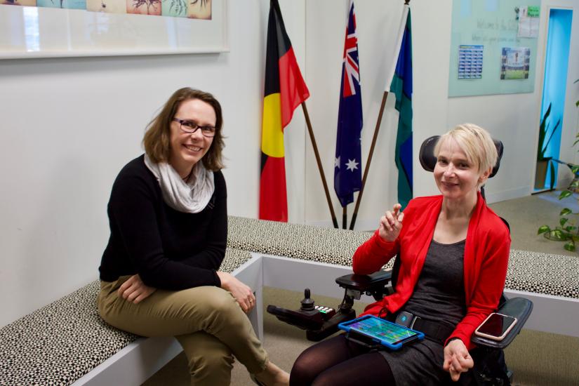 Female in wheelchair using communication device next to seated female.