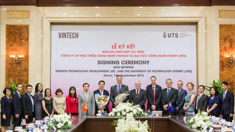 A group of people stand behind a floral arrangement in front of a celebratory banner