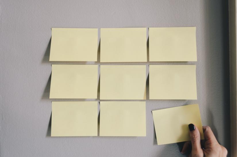 A female hand removes a yellow Post-it note from a grid of nine on a wall