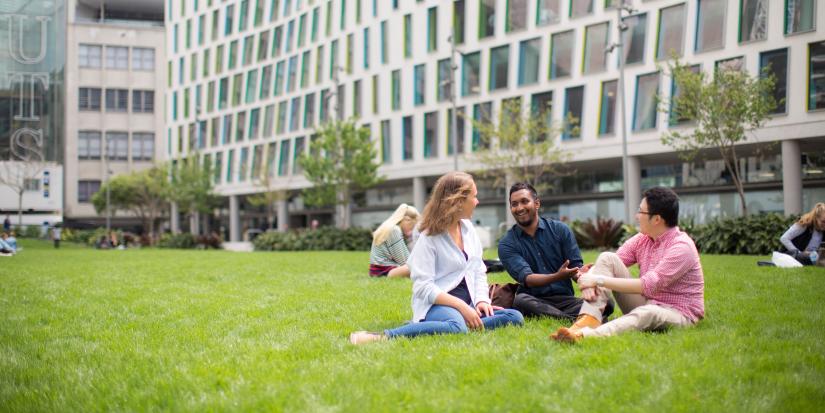 Three students talk sitting on the alumni green