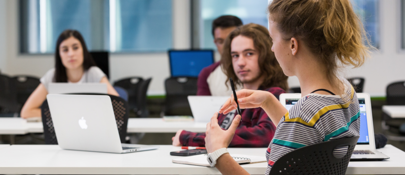 Four students in a classroom, with laptops and notebooks