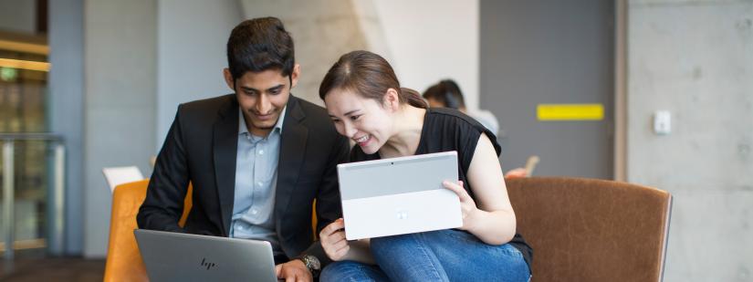 Two students sitting in a breakout space looking at their laptops