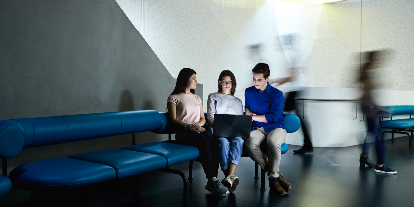 Three students sitting on a couch looking at a laptop