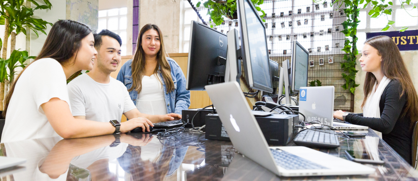 A group of students sitting at a desk looking at computer screens