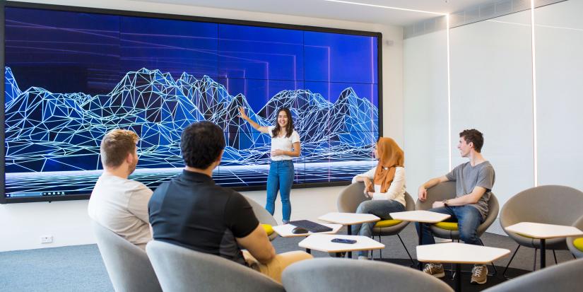 People looking toward a wall-sized screen where another person is pointing toward a data visualisation